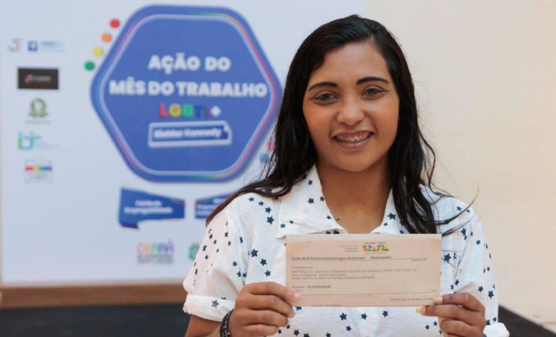 Mulher de cabelo preto segurando um papel e sorrindo para a câmera